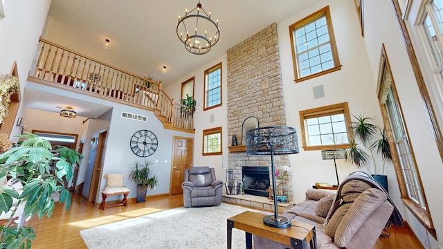 living room featuring visible vents, an inviting chandelier, a towering ceiling, wood finished floors, and a stone fireplace
