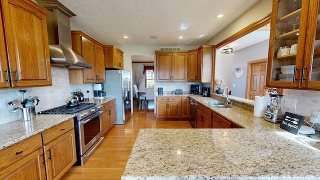 kitchen with wall chimney range hood, a sink, stainless steel appliances, backsplash, and visible vents
