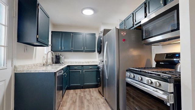 kitchen featuring light wood finished floors, a sink, stainless steel appliances, light countertops, and stacked washer and clothes dryer