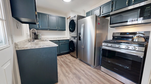 kitchen with a sink, light countertops, light wood-style floors, stacked washer / drying machine, and appliances with stainless steel finishes