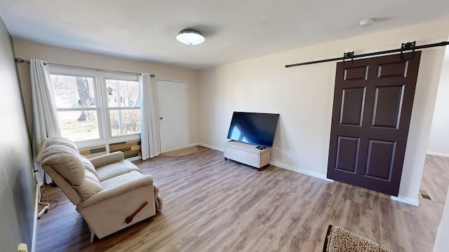 living area featuring a barn door, baseboards, visible vents, and wood finished floors