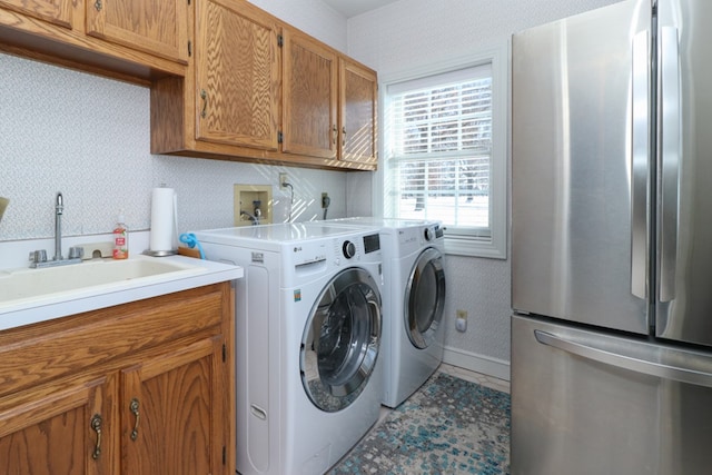 washroom with washing machine and clothes dryer, a sink, baseboards, wallpapered walls, and cabinet space