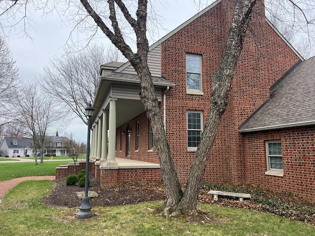 view of side of property featuring roof with shingles, brick siding, and a yard