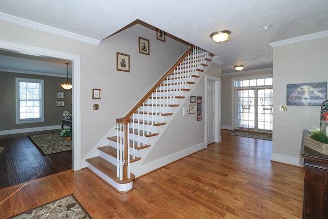 stairs with crown molding, wood finished floors, baseboards, and a healthy amount of sunlight