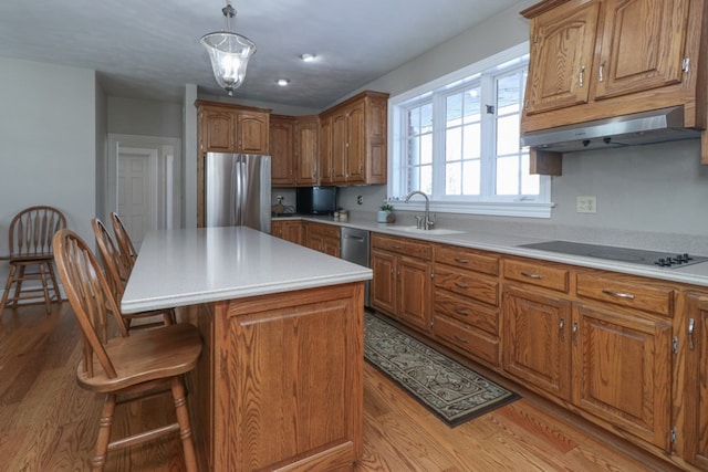 kitchen featuring a sink, freestanding refrigerator, under cabinet range hood, brown cabinetry, and black electric stovetop