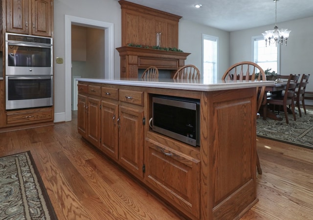 kitchen featuring a chandelier, brown cabinets, wood finished floors, and stainless steel appliances