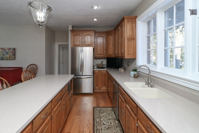 kitchen featuring light countertops, freestanding refrigerator, brown cabinetry, a sink, and wood finished floors