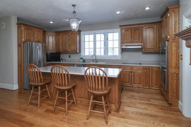 kitchen featuring a center island, a sink, light countertops, stainless steel appliances, and light wood-style flooring