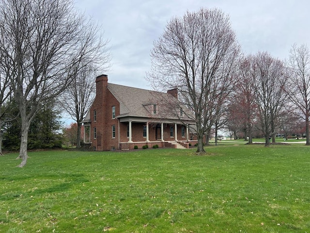 exterior space with a chimney, brick siding, a porch, and a yard