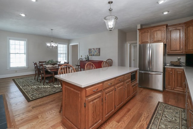 kitchen with decorative light fixtures, light countertops, appliances with stainless steel finishes, brown cabinetry, and a kitchen island