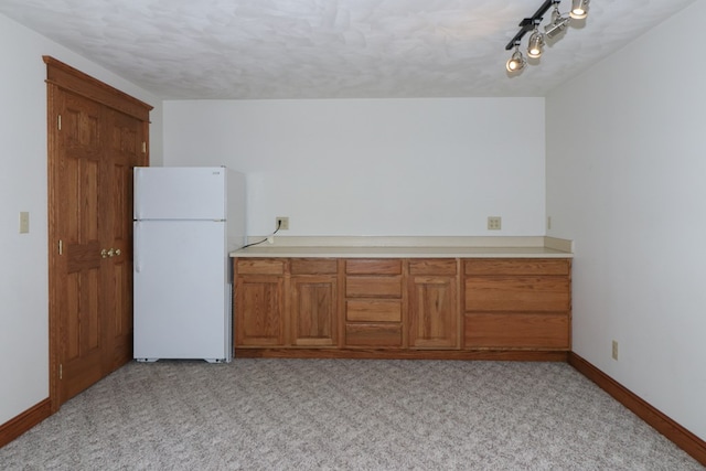 kitchen with brown cabinetry, light carpet, light countertops, and freestanding refrigerator
