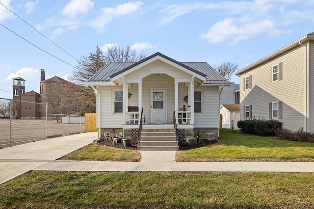 bungalow-style home featuring metal roof, fence, a front lawn, and a porch