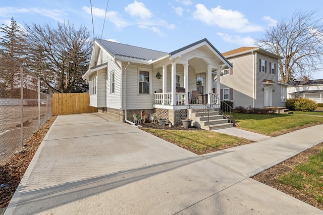 view of front of house with covered porch, metal roof, a front lawn, and fence