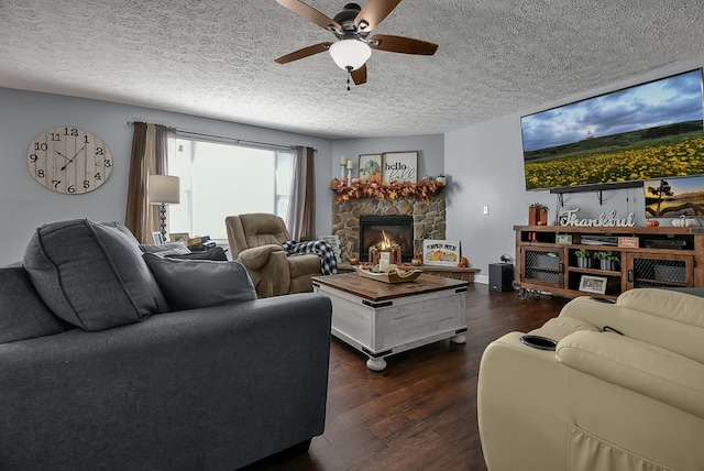 living room with a stone fireplace, ceiling fan, dark wood-type flooring, and a textured ceiling