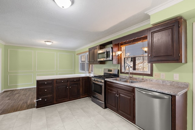 kitchen featuring a sink, stainless steel appliances, light countertops, dark brown cabinets, and a decorative wall