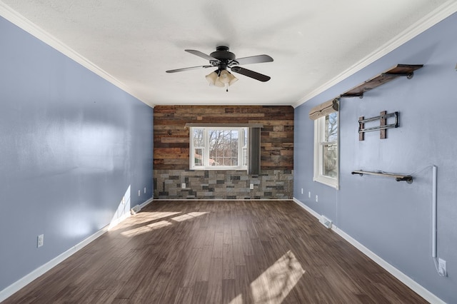 empty room with an accent wall, crown molding, baseboards, and wood finished floors