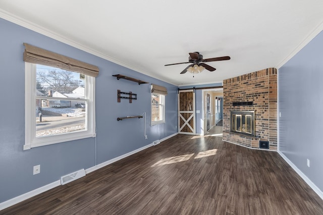 unfurnished living room with a barn door, wood finished floors, visible vents, and ornamental molding