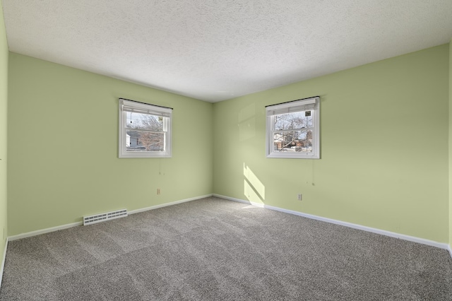 carpeted empty room featuring visible vents, a textured ceiling, and baseboards