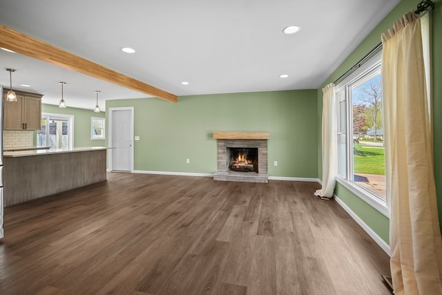 unfurnished living room with a brick fireplace, beam ceiling, baseboards, recessed lighting, and dark wood finished floors
