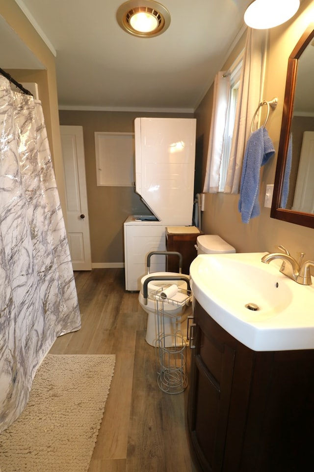 full bathroom featuring wood finished floors, vanity, baseboards, stacked washer / drying machine, and crown molding