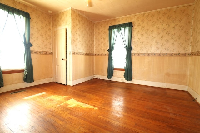 unfurnished room featuring a wainscoted wall, wood finished floors, visible vents, and wallpapered walls