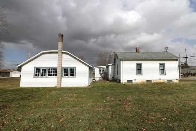 back of house featuring a chimney and a lawn