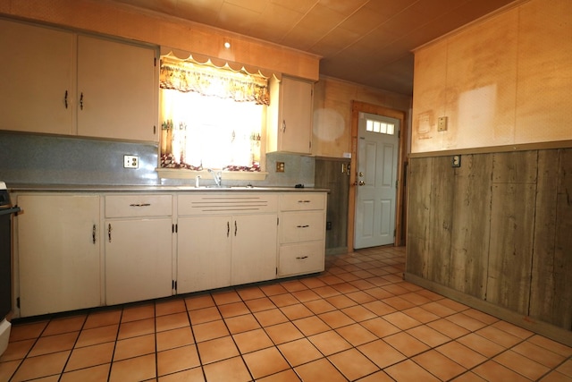 kitchen with light countertops, backsplash, white cabinets, a sink, and wooden walls