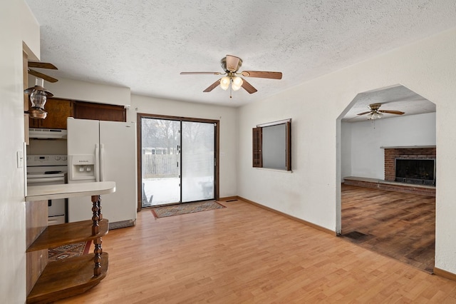 kitchen with white appliances, a brick fireplace, light hardwood / wood-style flooring, a textured ceiling, and ceiling fan