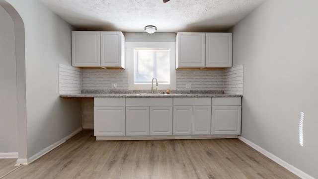 kitchen with white cabinetry, sink, backsplash, and light hardwood / wood-style floors