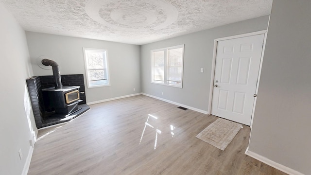 living room featuring light wood-type flooring, a textured ceiling, and a wood stove