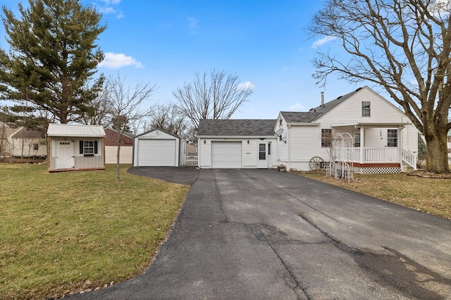 view of front of house with a detached garage, aphalt driveway, roof with shingles, an outdoor structure, and a front yard