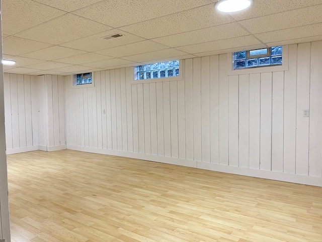 below grade area with visible vents, a paneled ceiling, baseboards, and wood finished floors