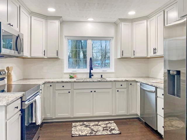 kitchen with dark wood-type flooring, a sink, appliances with stainless steel finishes, white cabinets, and light stone countertops
