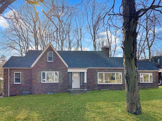 view of front of house with a front yard, brick siding, roof with shingles, and a chimney