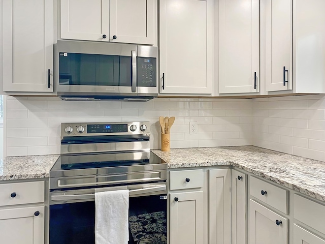 kitchen featuring backsplash, white cabinetry, stainless steel appliances, and light stone countertops