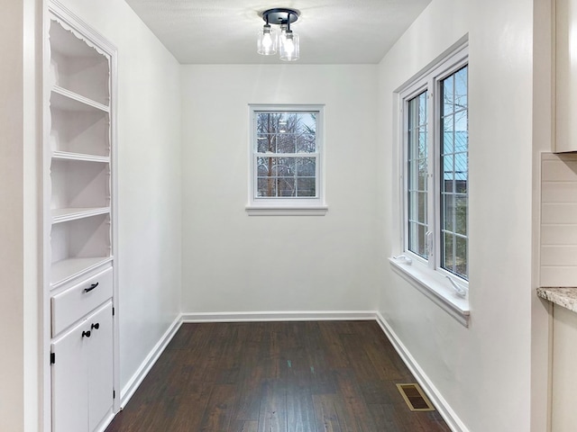 interior space with a wealth of natural light, visible vents, baseboards, and dark wood-style floors