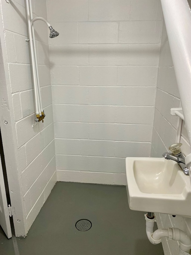bathroom featuring a tile shower, finished concrete floors, concrete block wall, and a sink