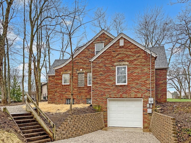 view of front of house with gravel driveway, a garage, brick siding, and roof with shingles