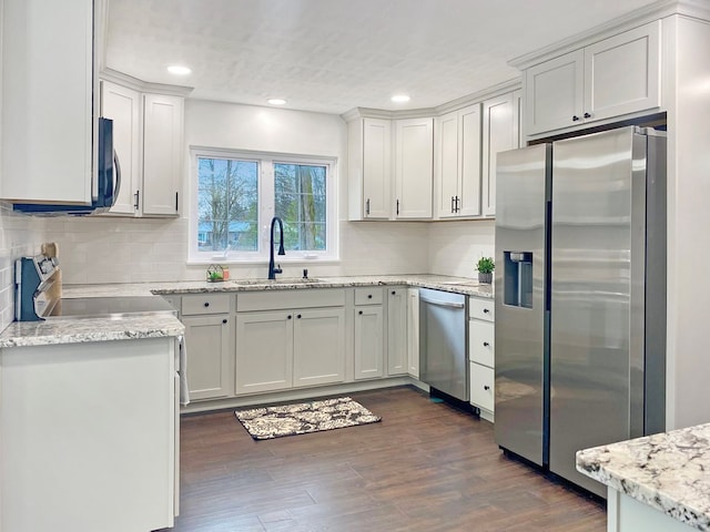 kitchen featuring a sink, backsplash, dark wood-style floors, appliances with stainless steel finishes, and light stone countertops