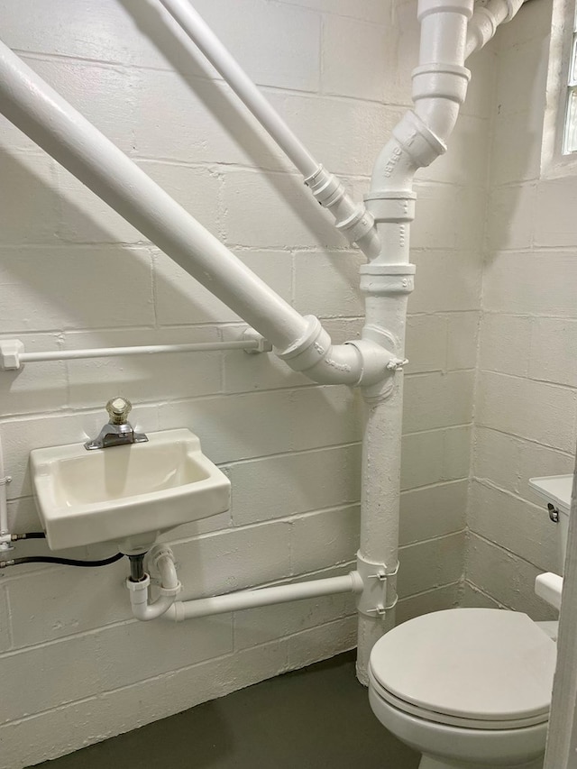 bathroom featuring toilet, concrete block wall, concrete floors, and a sink