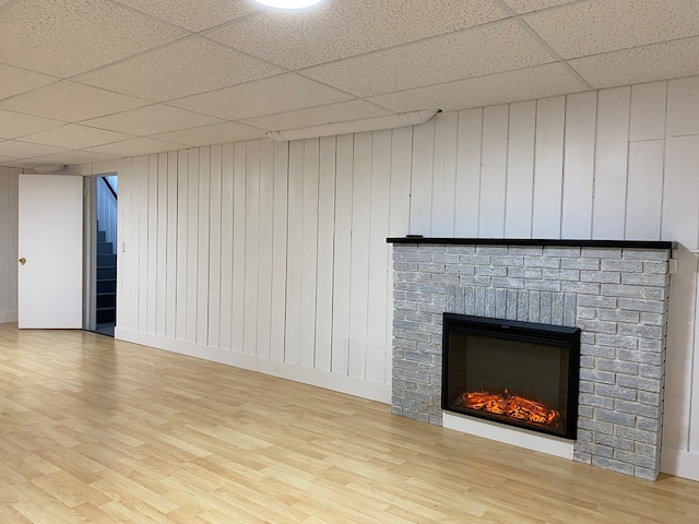 interior space with a brick fireplace, wood finished floors, and a paneled ceiling