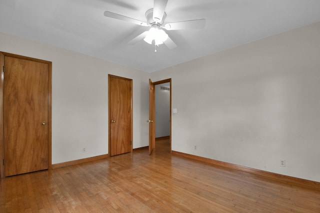 unfurnished bedroom featuring baseboards, light wood-style flooring, two closets, and a ceiling fan
