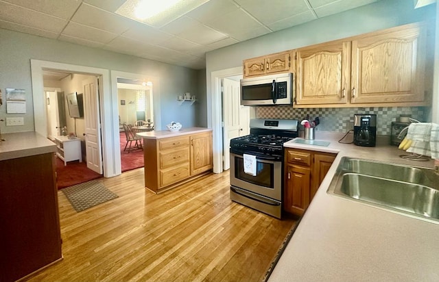 kitchen with sink, tasteful backsplash, a paneled ceiling, appliances with stainless steel finishes, and light wood-type flooring