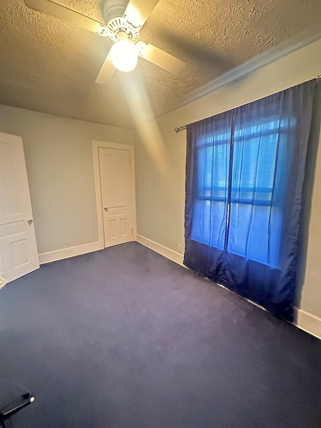 spare room with ceiling fan, dark carpet, and a textured ceiling