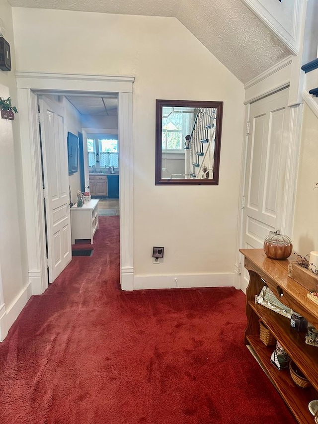 corridor with dark carpet, lofted ceiling, and a textured ceiling