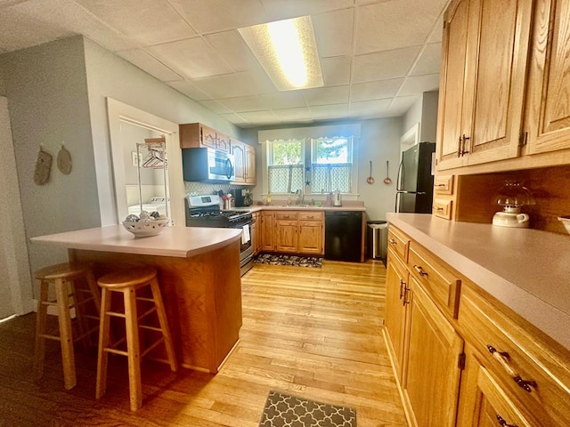 kitchen with a drop ceiling, backsplash, appliances with stainless steel finishes, light hardwood / wood-style floors, and a kitchen bar