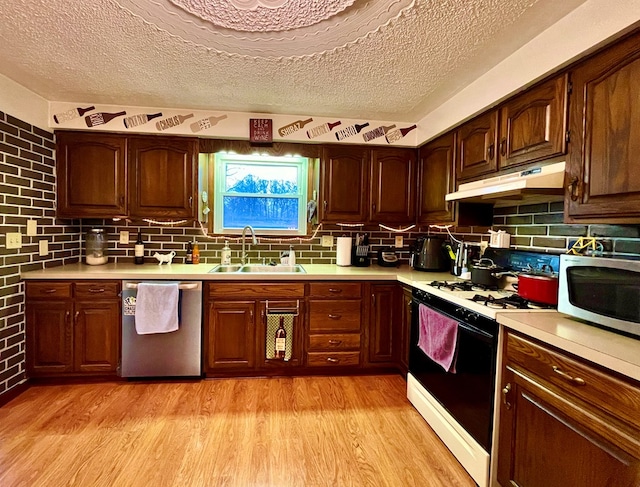 kitchen featuring appliances with stainless steel finishes, sink, backsplash, light hardwood / wood-style floors, and a textured ceiling