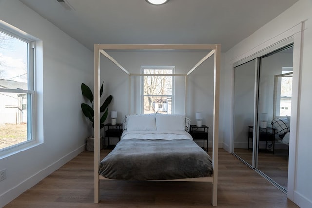 bedroom with multiple windows, visible vents, baseboards, and wood finished floors