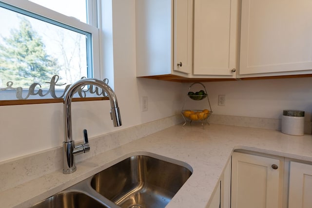 interior space with light stone countertops, plenty of natural light, white cabinets, and a sink