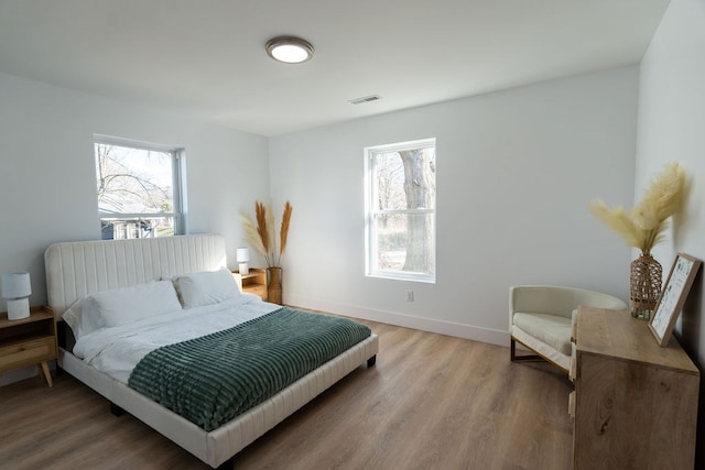 bedroom with light wood finished floors, visible vents, and baseboards